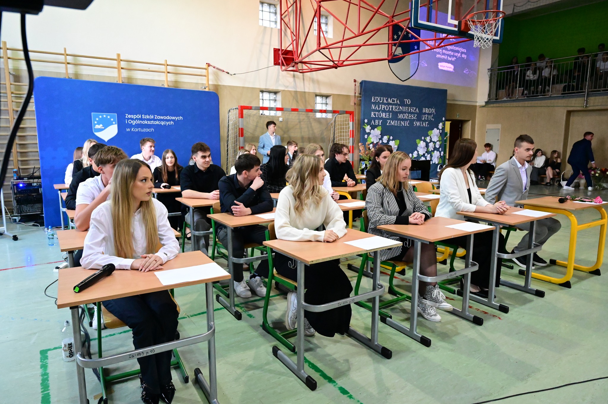 Uczniowie biorą udział w przedstawieniu - siedzą w szkolnych ławkach odgrywając scenę z lekcji